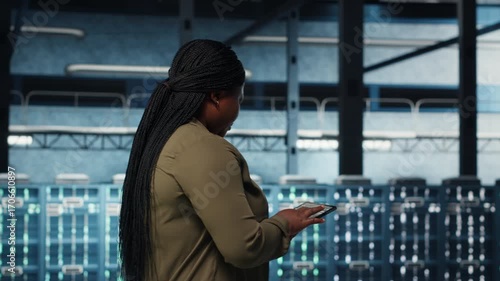 Smiling data center technician using tablet to manage software updates for system stability. Upbeat IT expert in server room configuring infrastructure with device for optimum performance, camera B