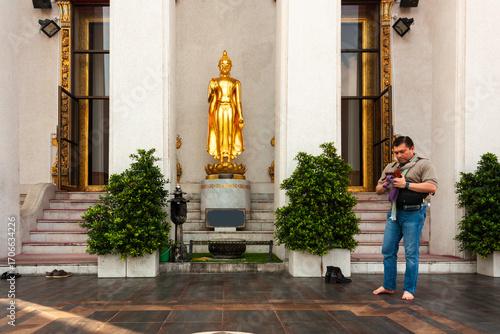 Caucasian barefoot man at buddhist temple in Bangkok, Thailand with golden buddha statue