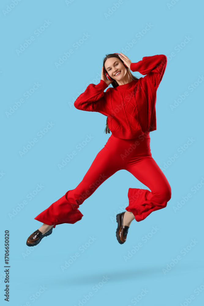 Fototapeta premium Young happy woman in headphones jumping on blue background