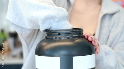 A woman scoops protein powder from a sports drink container. Sports nutrition and supplements.