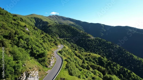 Aerial flyover of a winding road snaking through a green mountain range on a sunny day trees, exploration, winding road