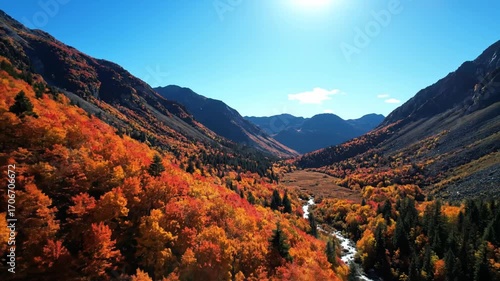 Aerial footage of a pristine, remote mountain range covered in autumn colors under a bright, sunny sky wilderness, warm colors, clear