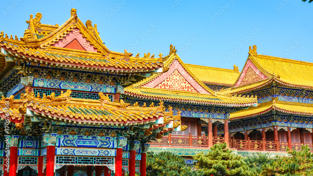 Naklejka premium Traditional Chinese temple in Penglai, Shandong, with red pillars, golden roofs, and ornate details, surrounded by lush greenery and a serene natural setting.
