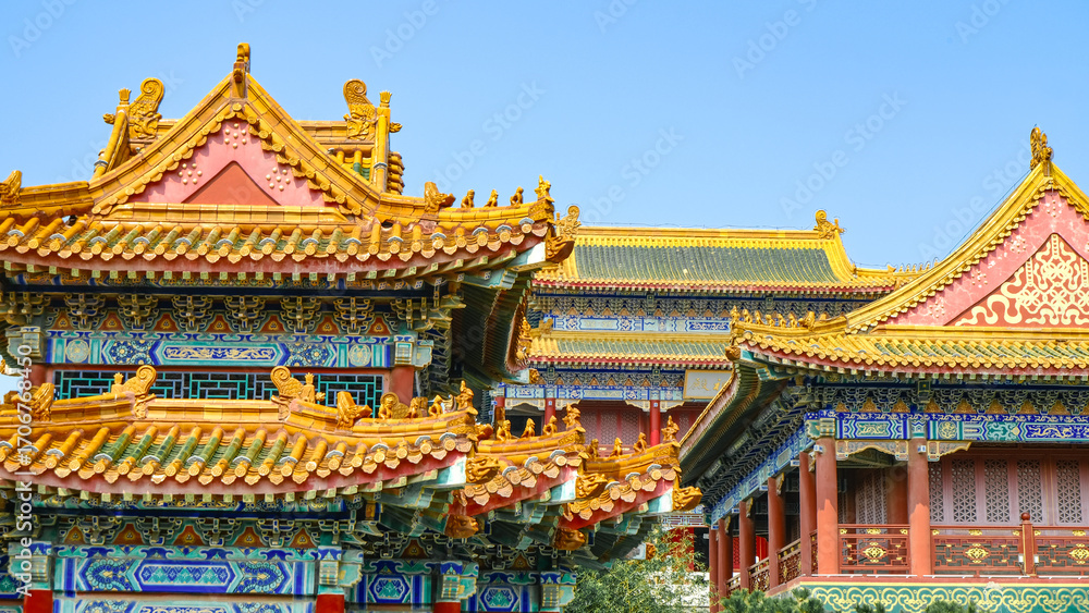 Naklejka premium Traditional Chinese temple in Penglai, Shandong, with red pillars, golden roofs, and ornate details, surrounded by lush greenery and a serene natural setting.
