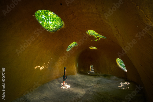 Woman Standing in Underground Cave Chamber with Natural Light and Green Vegetation
