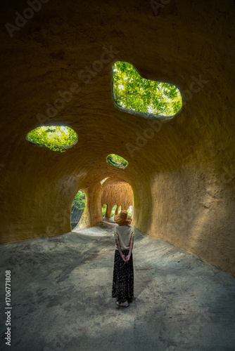 Woman Standing in Underground Cave Chamber with Natural Light and Green Vegetation