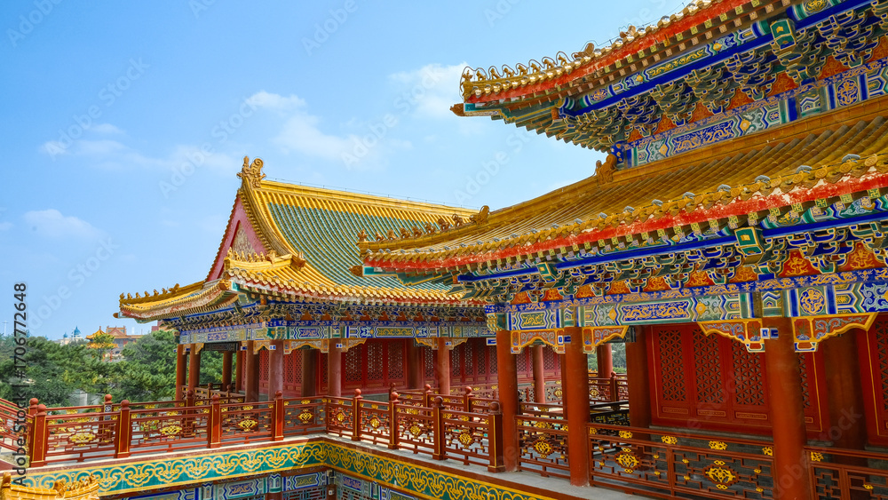 Naklejka premium Traditional Chinese temple in Penglai, Shandong, with red pillars, golden roofs, and ornate details, surrounded by lush greenery and a serene natural setting.
