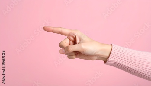 A pale hand, adorned with a pink sweater, points left against a solid pink backdrop. The focus is on the outstretched index finger