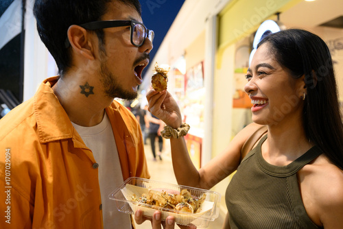 Happy couple sharing takoyaki in a food court
