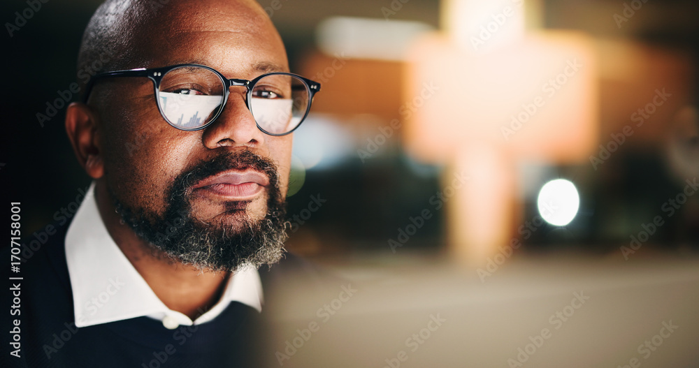 Fototapeta premium Computer, finance and night with business black man in office for portfolio or risk management. Face, glasses reflection and space with mature employee reading financial charts or graphs in evening