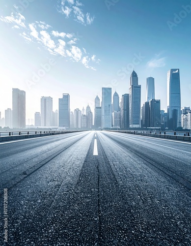 Asphalt road stretches into a skyline of towering buildings under a sunny sky, conveying urban expansion and infrastructural development