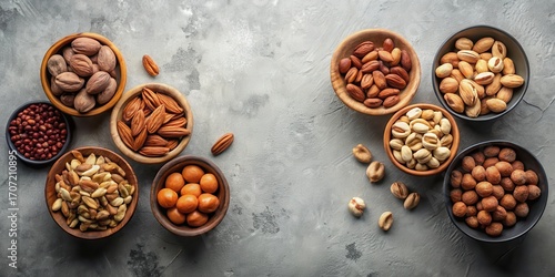 An assortment of shelled nuts in various wooden and dark gray bowls on a textured gray surface, showcasing almonds, pistachios, and other types of nuts