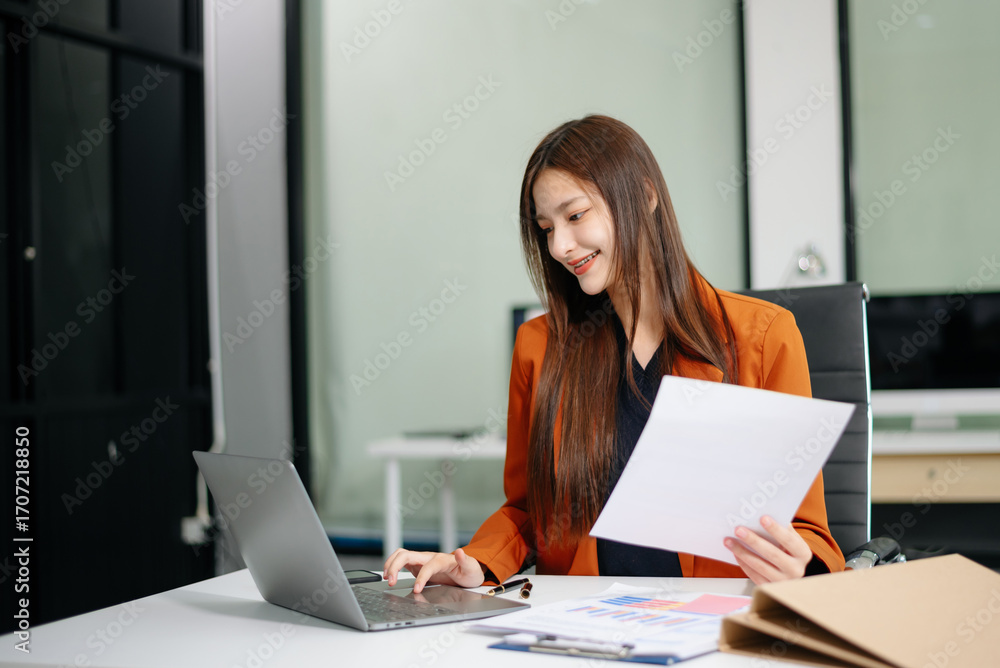 Fototapeta premium Confident businesswoman working on a laptop at a sleek office desk, showcasing professionalism, productivity