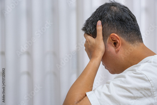 Middle-aged Asian man holding head in stress, showing signs of work-induced headache. Ideal for ads on migraine, mental health, and neurological care.