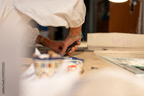 Gros plan sur une femme artisan vitrailliste en train de manipuler des vitraux dans son atelier, montrant précision et savoir-faire.