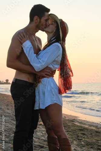 Happy young couple tenderly embracing and kissing at the beach at sunset.