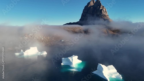Town Uummannaq during summer in northern West Greenland beyond the Arctic Circle. Greenland, Danish territory. Large mountains and glaciers in the background. Misty morning. Fjord in Greenland. Aerial