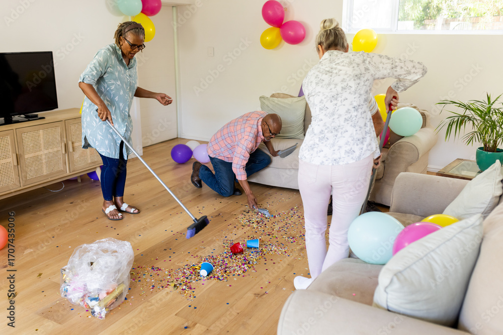 Fototapeta premium Senior friends cleaning up colorful confetti after fun indoor celebration