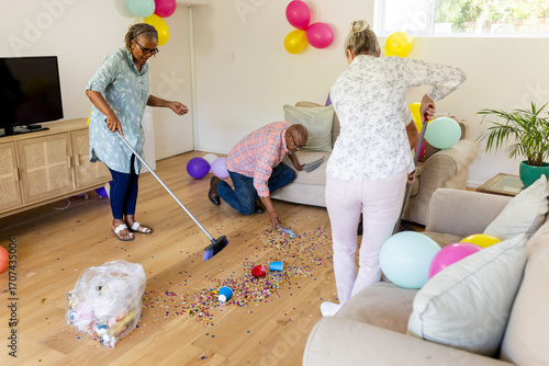 Senior friends cleaning up colorful confetti after fun indoor celebration