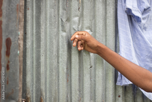 A persons arm reaches out towards a corrugated metal wall with laundry hanging