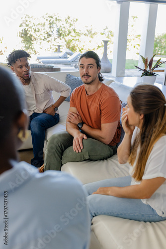 Diverse friends sitting on couch at home, engaging in lively conversation