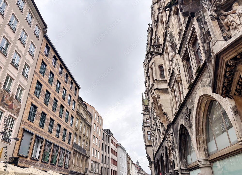 Obraz premium A view up at the various architectural styles of different eras of buildings in the historical part of Munich while walking along quiet, cozy streets on a cloudy rainy summer day.