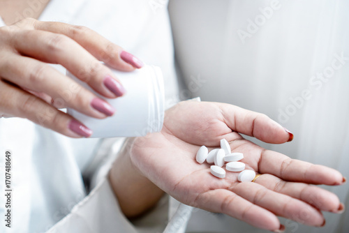Close-up of a woman’s hand holding a bottle of medicine while taking pills. Concept of overdose risk with paracetamol or painkillers, medication use, and health care awareness