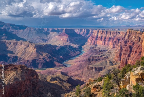 Expansive vista of the Grand Canyon with river winding through the layers of red and brown rock formations under a partly cloudy sky