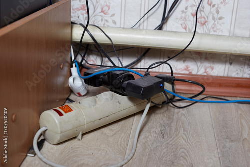A white power strip with multiple plugged-in devices lies on a wooden floor