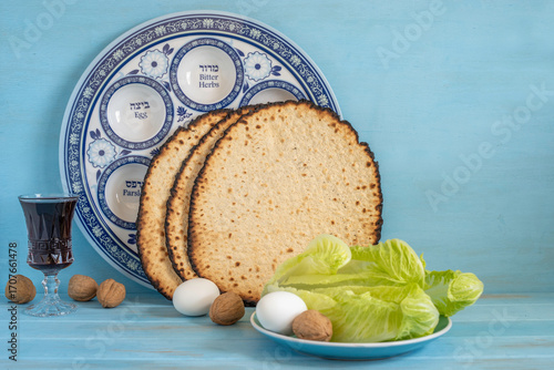 Jewish holiday Pesach or Passover concept with symbolic food (eggs, walnuts, lettuce leaves, matzah) on the background of traditional Seder Plate and blue wood background.