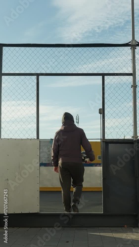 Wallpaper Mural Back view of man walking away from urban sports arena, carrying a soccer ball, with vibrant yellow storage containers and city buildings in the background Torontodigital.ca