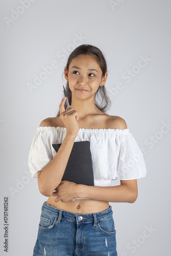 Girl is standing with a thoughtful expression, holding a dark book or tablet 