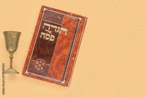 Jewish holiday Pesach (Passover) concept with Kiddush cup, traditional book with text in Hebrew: 
