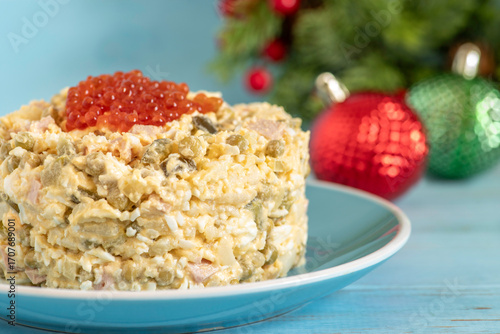 Russian potato salad Oliver for Winter holidays, for New Year made of boiled eggs, potato, chicken, cucumber served with red caviar on blue ceramic plate.
