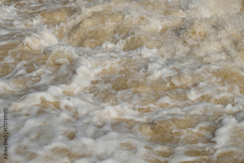 Obraz na plátně Background texture of a murky brown and foamy river flow
