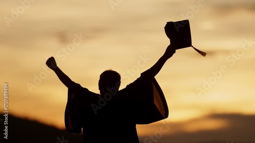 Silhouette of a proud graduate lifting graduation cap during sunset. Concept of achievement, celebration, and new beginnings.