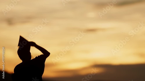 Inspirational silhouette of a graduate lifting graduation hat in sunset, symbolizing fulfilled academic dreams and bright beginnings.