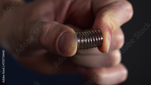 A compressed steel spring in a person's hands.
Pressure on the spring with hands.
A man holds a shock-absorbing spring and compresses it with his fingers.
Spring, pressure, steel, part