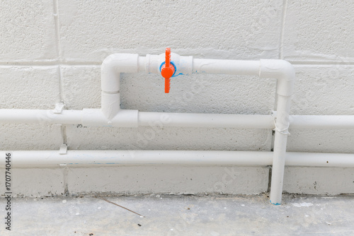 White plumbing pipe detail with an orange valve for water supply during house construction or renovation project. clean and functional system on concrete wall background