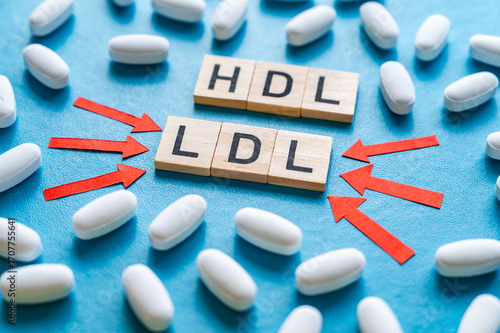Concept of the difference between HDL and LDL cholesterol, words composed with wooden alphabet on a blue background, and drug tablets surrounding them; bad LDL cholesterol.