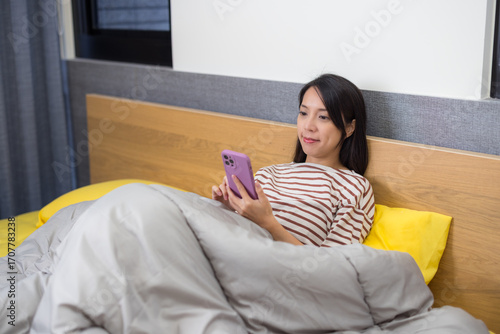 Woman lying down in bed looking at phone
