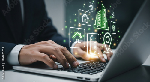 Hands on a laptop keyboard with a futuristic holographic display showing real estate and smart city icons, illustrating property technology and urban development