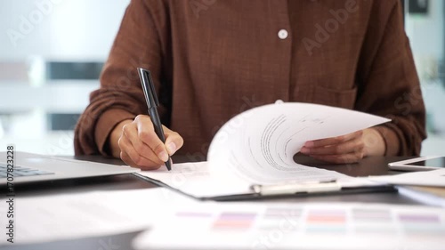 Close up of female hand signing documents at a desk at a workplace in a business office. Confident businesswoman manager looks through the folder with documentation and signs the contract with a pen
