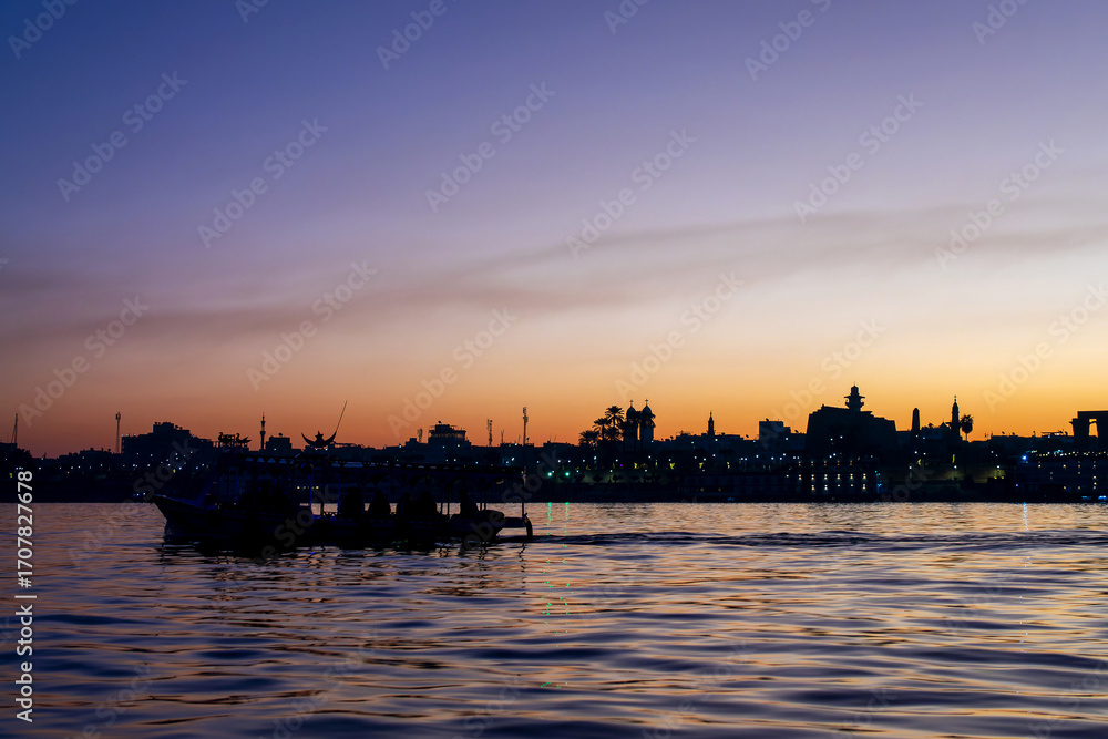 Fototapeta premium Silhouette of a motorboat egyptian ferry on the Nile river, Luxor East bank at sunrise, Egypt