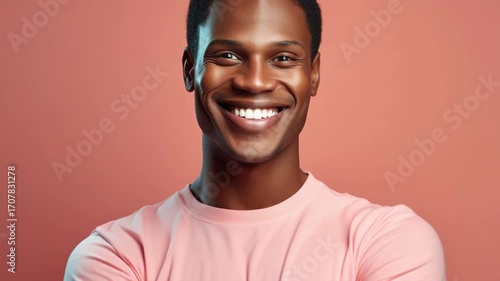 Young athletic man in pink shirt smiling towards camera with hands on hips.