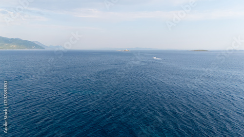 The ocean is calm and clear, with a few boats in the distance