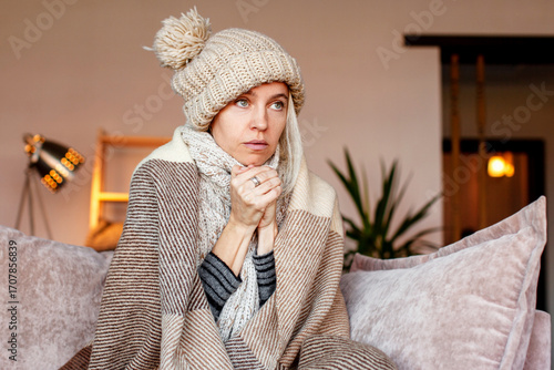 Woman warmly clothed and hat in a cold home sitting on couch