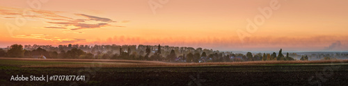 Panorama of a field with silhouettes of trees, buildings in the distance on t...