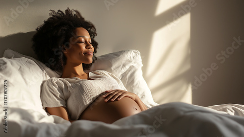 Pregnant Black woman wakes up and stretches peacefully in bed during morning sunlight