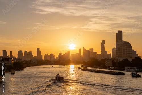 Golden sunrise over Chao Phraya River in Bangkok with boats and city skyline in the background of the Thai capital.